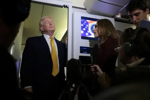 دونالد ترامب يقف أمام باب الطائرة، بينما تتحدث صحفية إليه، محاطًا بعدد من الصحفيين، مع شاشة تعرض شعار الحكومة الأمريكية في الخلفية.