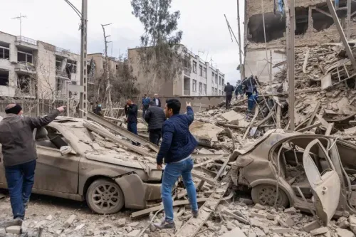 مشهد لرجال يتفقدون الأضرار في منطقة مدمرة بعد قصف، مع سيارات مدمرة وأنقاض مبانٍ، يعكس تأثير الحرب في إيران.