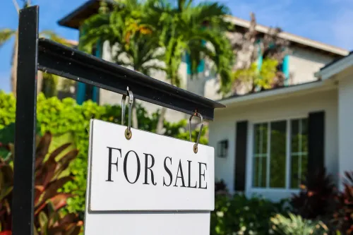 لافتة "للبيع" أمام منزل محاط بالنباتات، تشير إلى تحسن محتمل في سوق الإسكان الأمريكي في عام 2026.