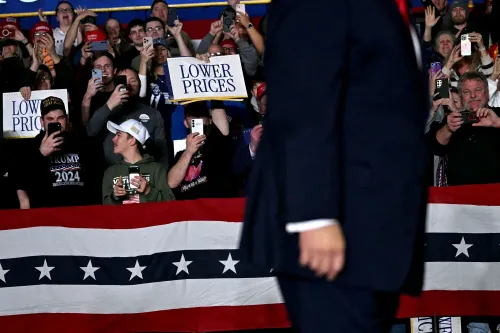 حشود من مؤيدي ترامب في تجمع انتخابي، يحملون لافتات تطالب بخفض الأسعار، بينما يتقدم ترامب نحو المنصة.