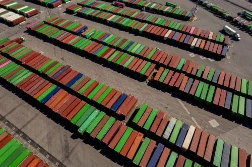 صورة جوية لمستودع يحتوي على حاويات شحن ملونة، تمثل تدفق التجارة والاقتصاد الأمريكي وتأثير التعريفات الجمركية على الصناعة.