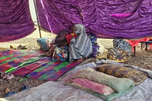 امرأة جالسة تحت خيمة مؤقتة، تعبر عن القلق وسط أكياس وأقمشة ملونة، تعكس معاناة النازحين في السودان بسبب الحرب الأهلية.