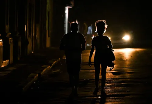 شخصان يسيران في شارع مظلم في هافانا، مع إضاءة خافتة من السيارات، مما يعكس الأجواء الصعبة التي يعيشها الكوبيون.