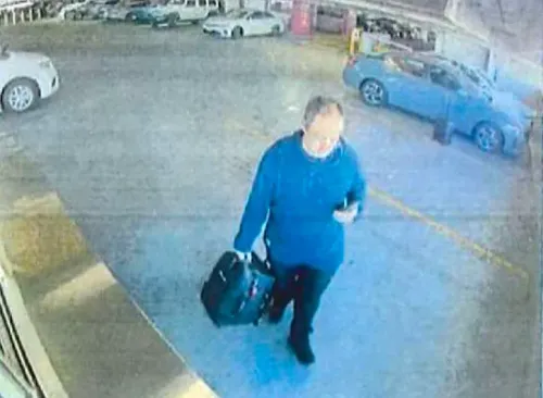 رجل يحمل حقيبة سوداء ويستخدم هاتفه المحمول، يظهر في موقف سيارات، خلفه سيارات متوقفة، في سياق تحقيقات حول إطلاق نار في جامعة براون.