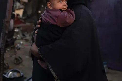 امرأة تحمل طفلًا صغيرًا في حضنها، تعكس مشاعر الأمل والرعاية وسط ظروف صعبة في غزة، حيث تواجه النساء تحديات الحياة اليومية.