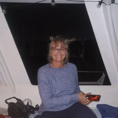 امرأة مبتسمة ترتدي سترة زرقاء وتجلس في قارب، تحمل هاتفًا، وسط أجواء مظلمة، في سياق حادث غرق بجزر البهاما.