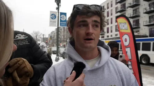 شخص يتحدث في الشارع خلال طقس بارد، محاط بأعلام ولافتات، في سياق جدل حول الاحتيال في مراكز رعاية الأطفال بمينيسوتا.