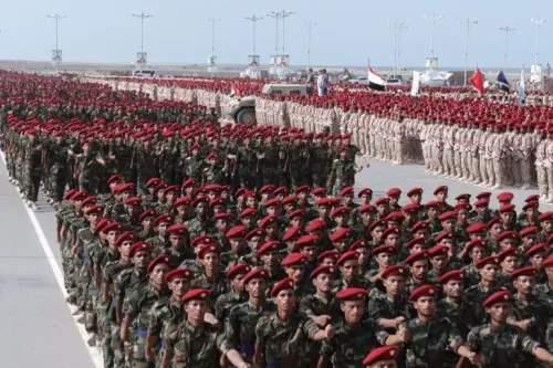 تجمع حشود من الجنود اليمنيين في عرض عسكري، يرتدون زيًا موحدًا وقبعات حمراء، في سياق تصاعد التوترات الإقليمية.