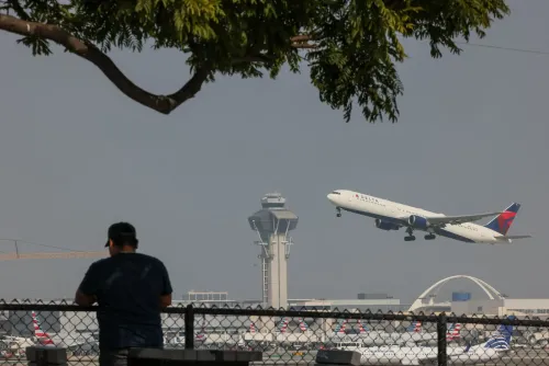 طائرة دلتا تقلع من مطار مزدحم، بينما يقف شخص على السياج، مشاهدًا الحركة الجوية. تعكس الصورة الفجوة بين المسافرين الأثرياء والاقتصاديين.