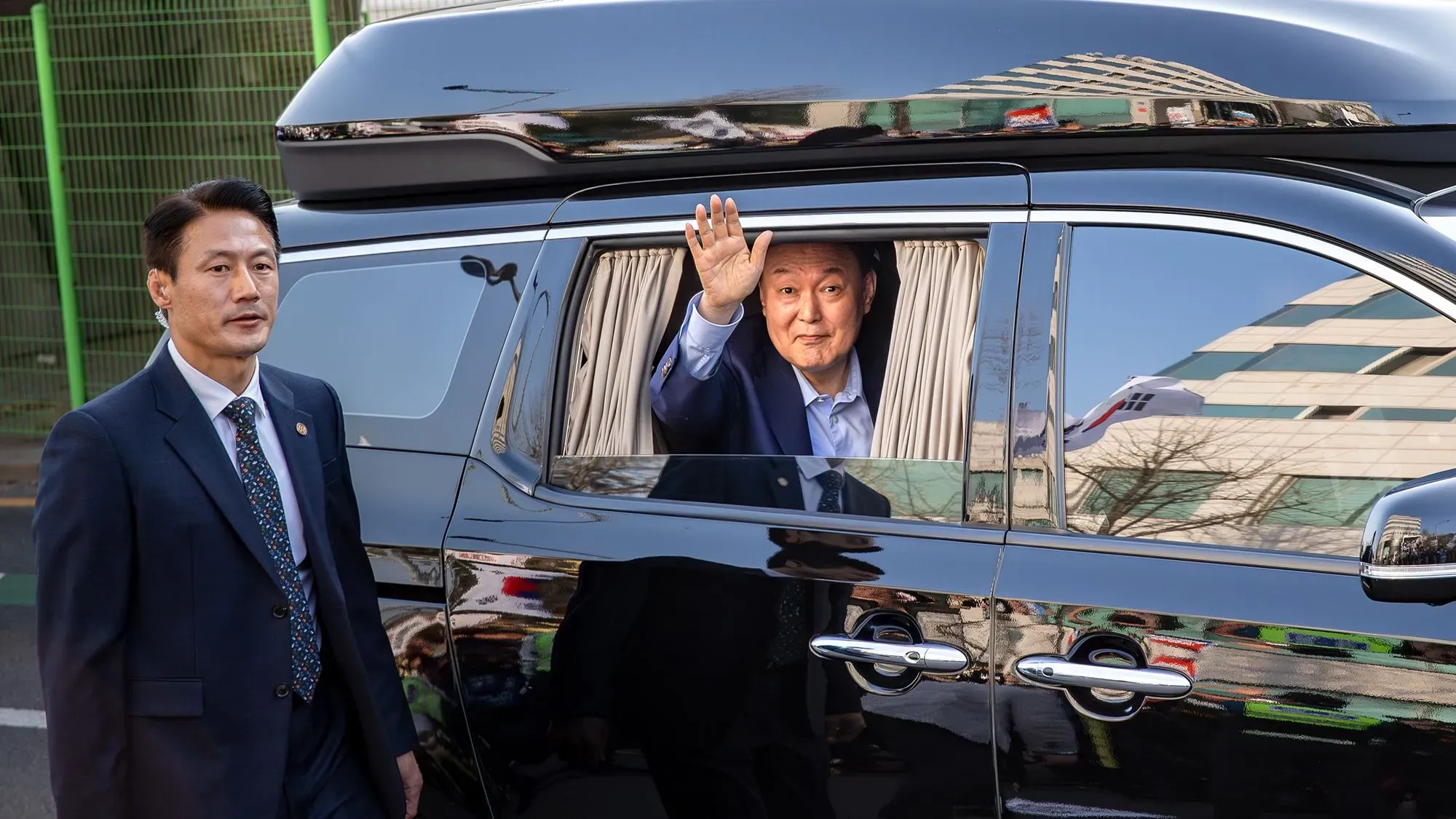الرئيس الكوري الجنوبي السابق يون سوك يول يلوح بيده من نافذة سيارته، يرافقه حارس شخصي، بعد عودته إلى منزله في سيول.