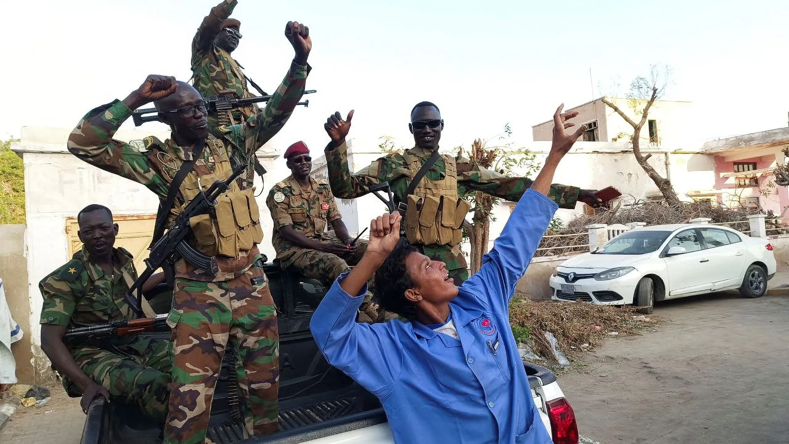 جنود من الجيش السوداني يحتفلون في ود مدني بعد استعادة السيطرة على المدينة من قوات الدعم السريع، مع تواجد مركبات مدنية خلفهم.