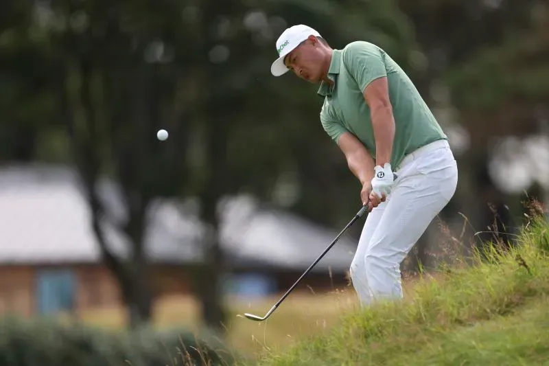 لاعب الجولف هاوتونغ لي يستعد لتسديدة من العشب الطويل أثناء البطولة المفتوحة، مع التركيز على الكرة في الهواء.