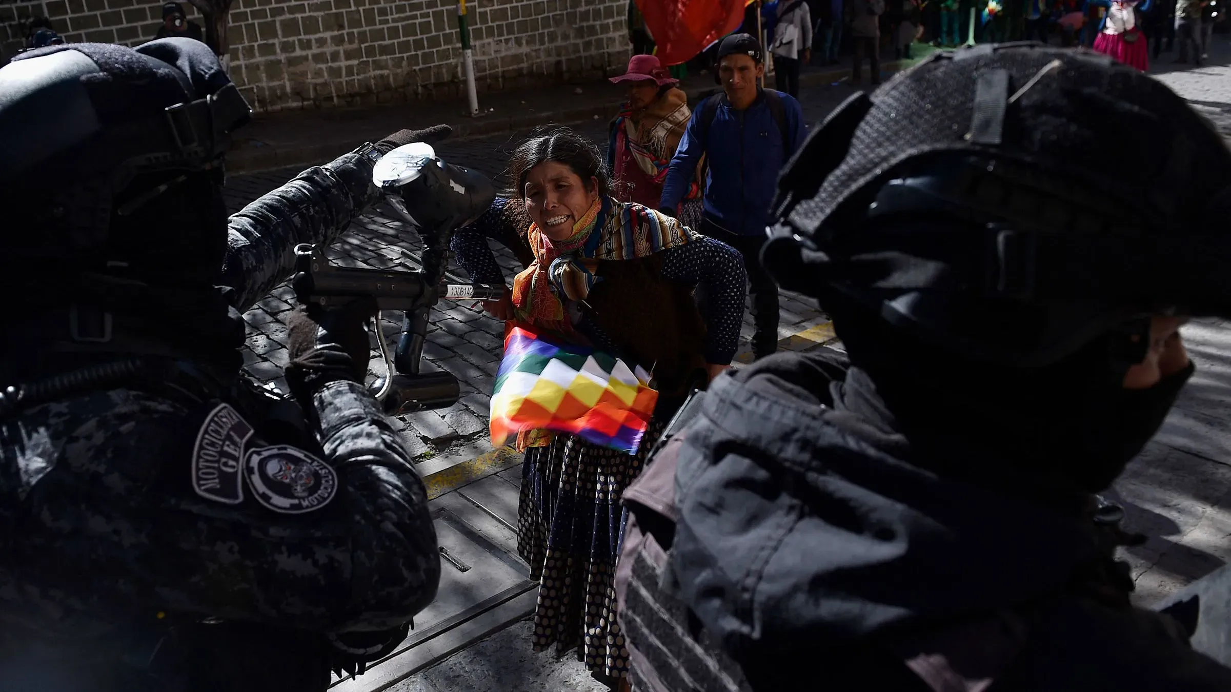 مؤيدة لإيفو موراليس تتفاعل مع قوات الأمن خلال مسيرة في لاباز، حاملة علم بوليفيا، وسط توترات سياسية واشتباكات.