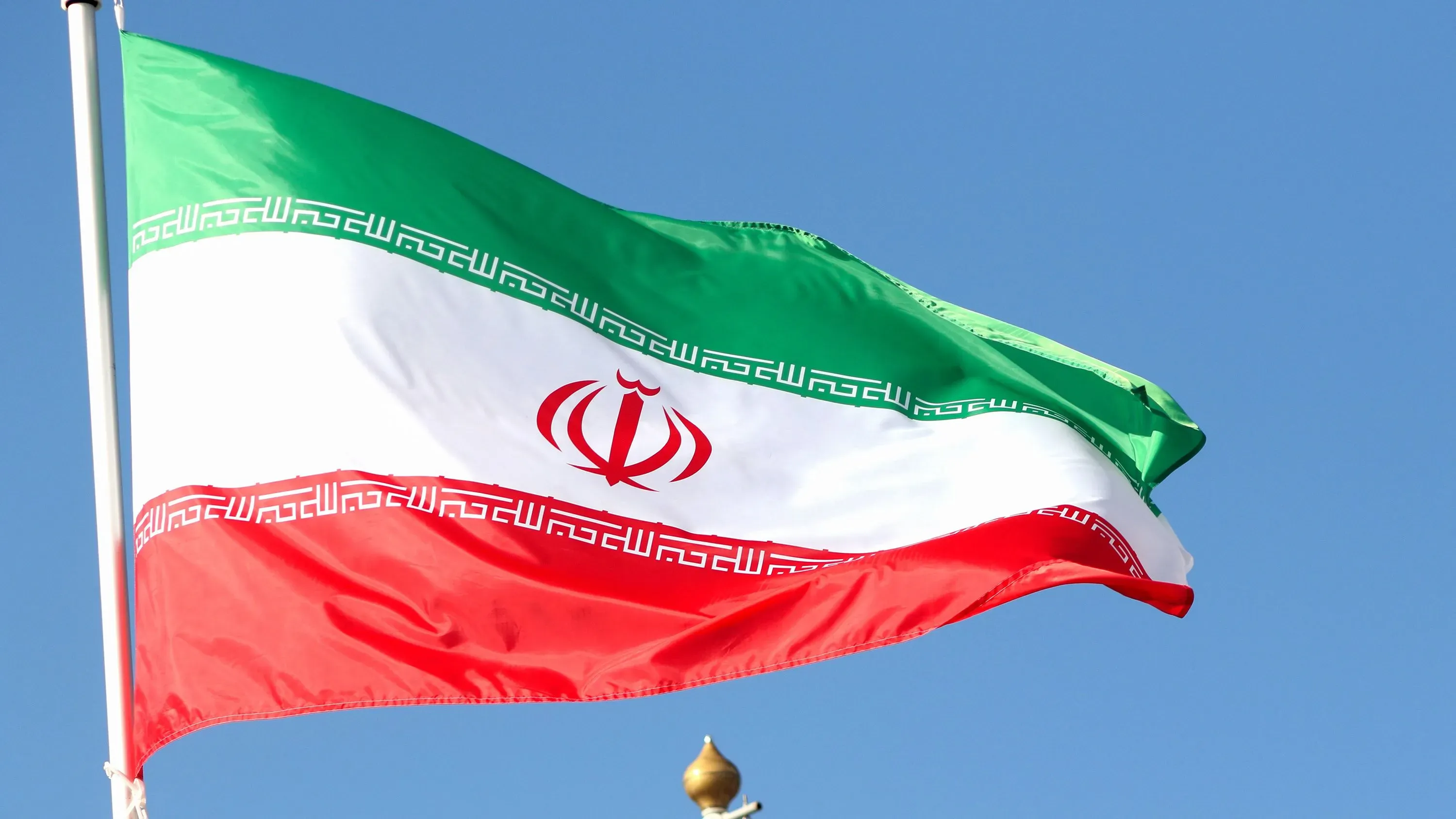علم إيران يرفرف في السماء الزرقاء، مع ظهور رموز وطنية واضحة، في سياق الأحداث المتعلقة بوفاة مواطن سويسري في السجن.