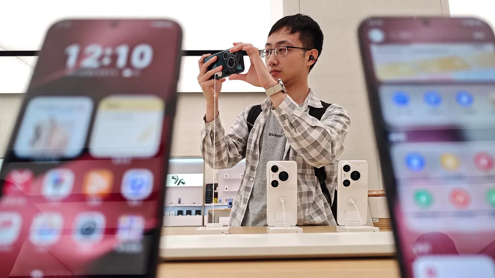 شاب يحمل هاتفًا ذكيًا في متجر، مع عرض هواتف أخرى في المقدمة. تعكس الصورة التوجهات الحديثة في صناعة التكنولوجيا.