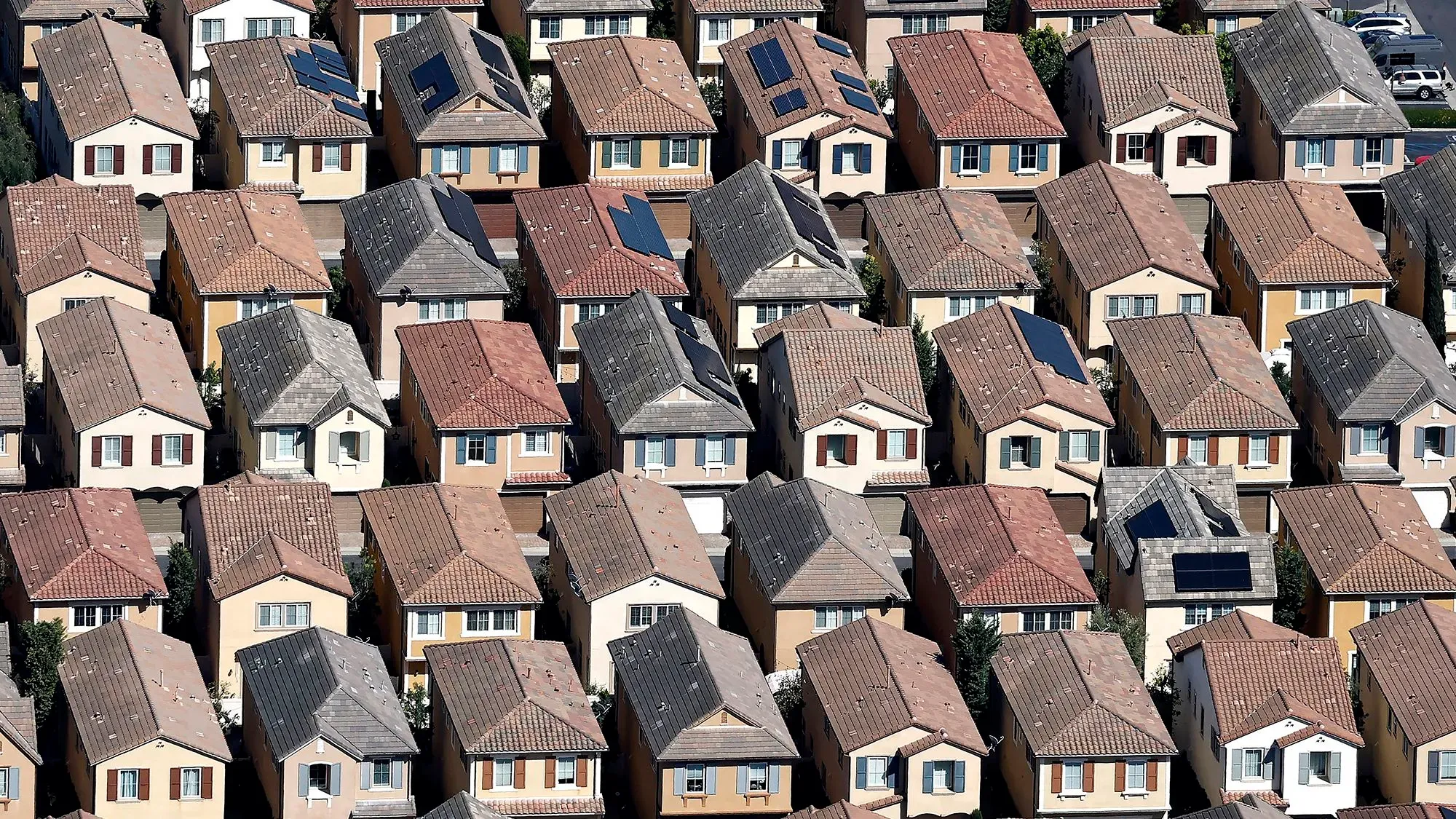 تظهر الصورة مجموعة من المنازل المتجاورة في حي سكني، مع أسطح مائلة وبعضها مزود بألواح شمسية، مما يعكس حالة سوق العقارات الحالي.