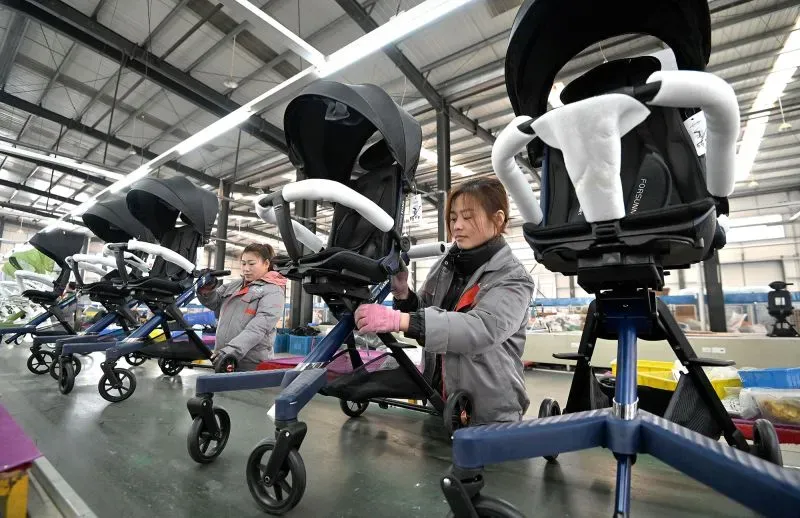 عمال في مصنع يقومون بتجميع عربات الأطفال، مع التركيز على تأثير التعريفات الجمركية على أسعار مستلزمات الأطفال.