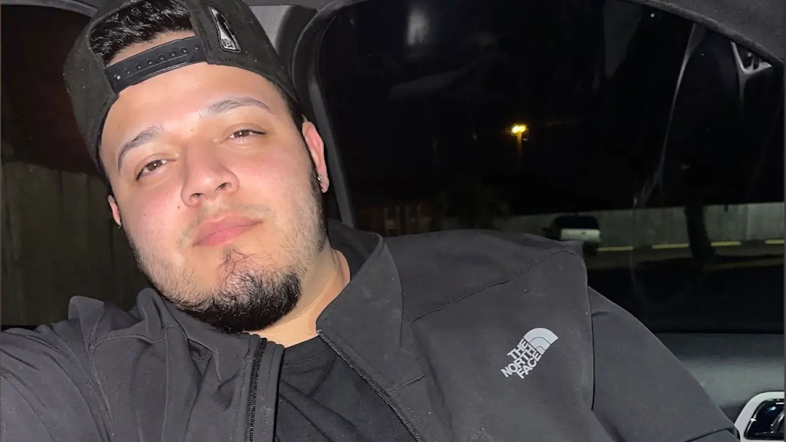 صورة لرجل يجلس في سيارة، يظهر وشم على أصابعه يتضمن صليبًا وجمجمة ووجهًا مبتسمًا، مما يثير جدلًا حول ارتباطه بعصابة MS-13.