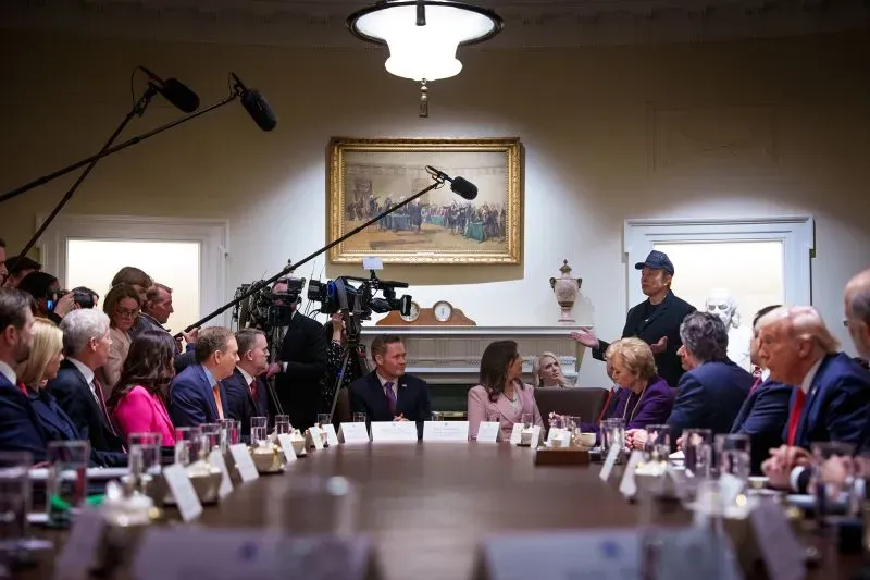 اجتماع في البيت الأبيض مع إيلون ماسك وسط مجموعة من المسؤولين، حيث يتحدث بحضور كاميرات الإعلام.