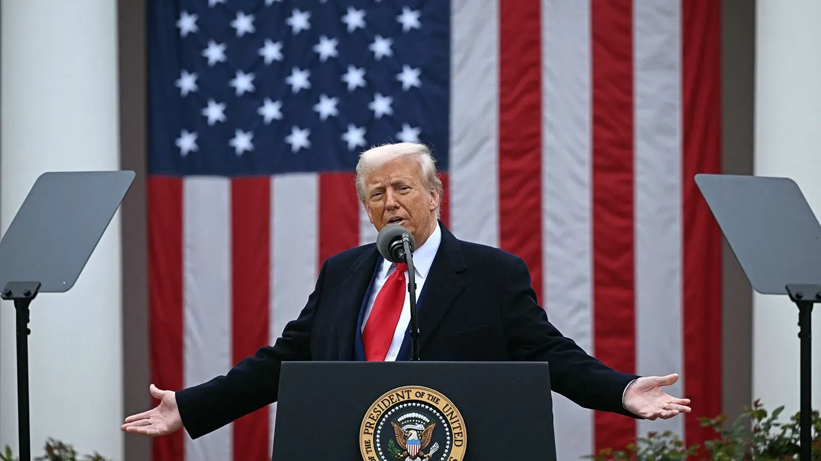 دونالد ترامب يتحدث في مؤتمر صحفي، مع العلم الأمريكي خلفه، حيث يناقش تأثيرات سياساته على الاقتصاد.
