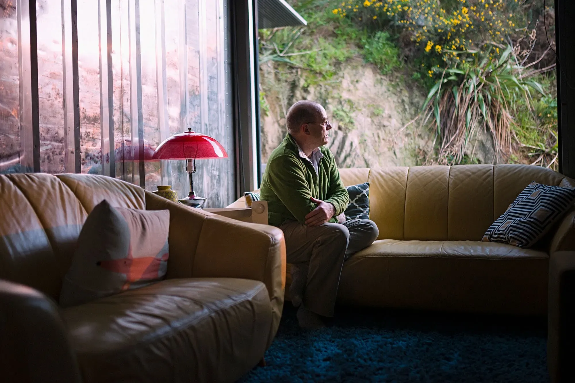 رجل مسن يجلس بمفرده على أريكة في غرفة مضيئة، يبدو عليه التأمل والقلق، مما يعكس تأثير الاكتئاب على الصحة العقلية.