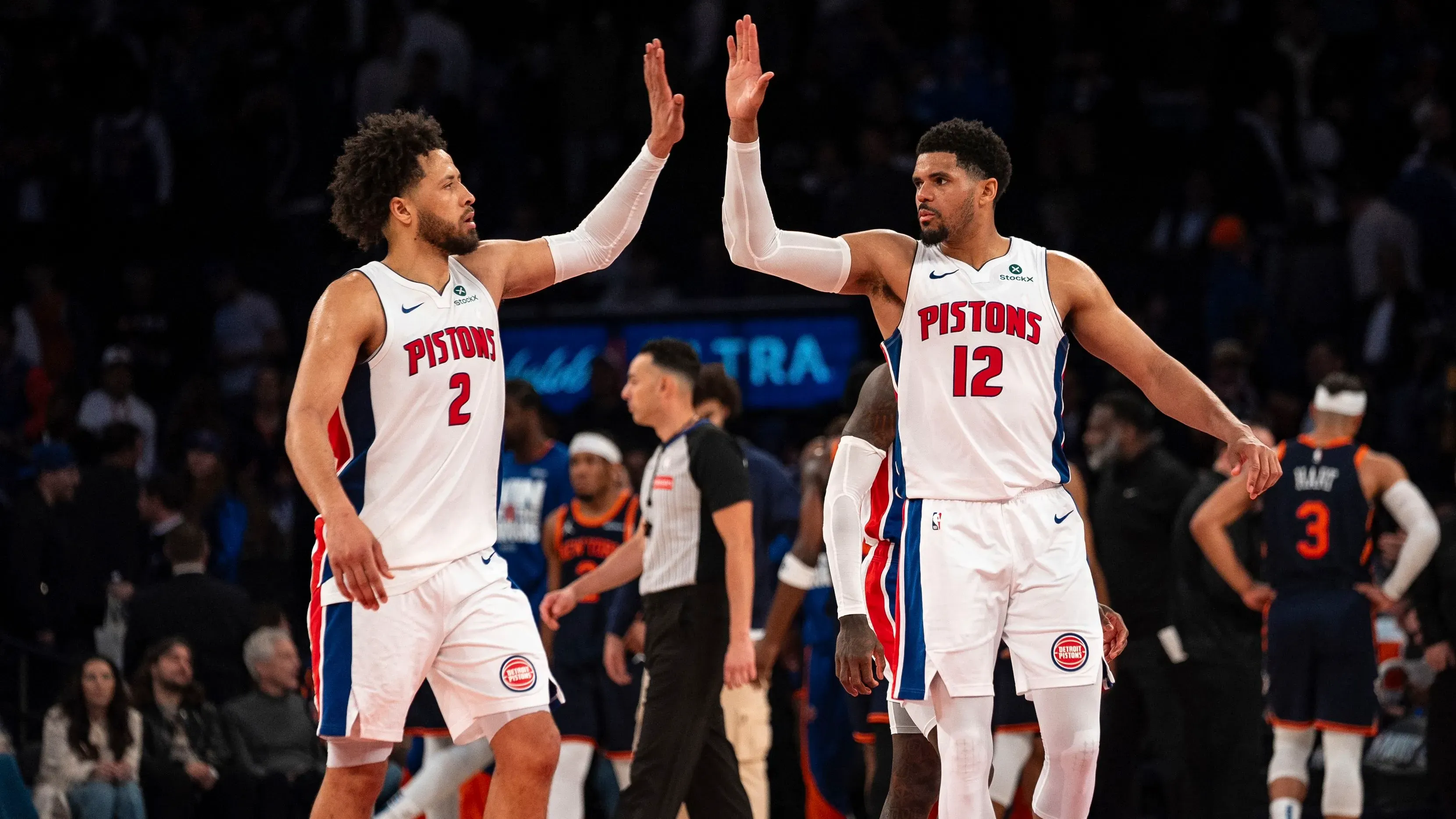 يظهر لاعبا فريق ديترويت بيستونز، كيد كانينغهام وتوباس هاريس، يتبادلان التحية خلال مباراة، مما يعكس روح الفريق والتفاؤل في موسمهم الجديد.