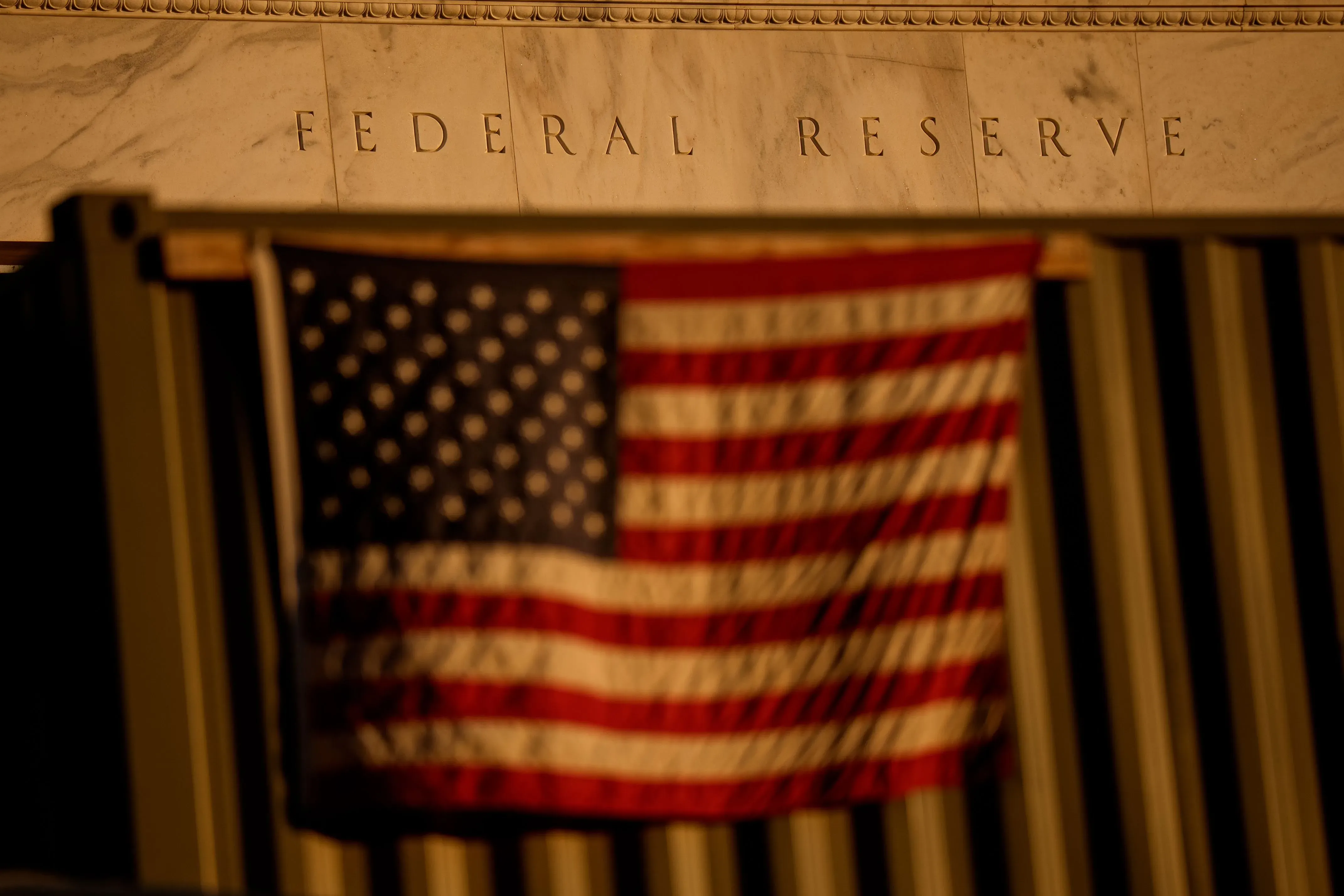 واجهة بنك الاحتياطي الفيدرالي مع علم الولايات المتحدة، تعكس التوترات الاقتصادية والسياسات النقدية في ظل التضخم.