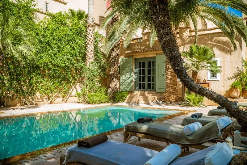 فناء جميل في تارودانت مع بركة سباحة محاطة بأشجار النخيل، يمثل أجواء الاسترخاء في المدينة المغربية التقليدية.