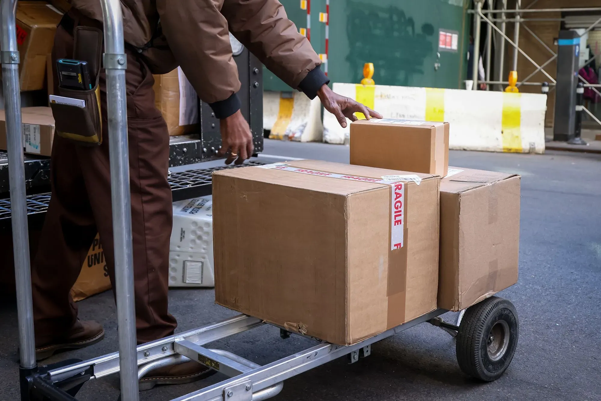 عامل توصيل يحمل صناديق على عربة في منطقة حضرية، مما يعكس تأثير سوق العمل المتراجع في الولايات المتحدة.