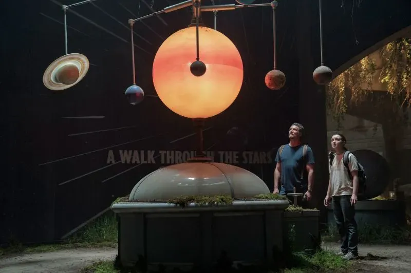 جويل وإيلي يتأملان نموذجًا شمسيًا في متحف، يعكسان لحظة دافئة في حلقة "The Last of Us" التي تستكشف علاقتهما.