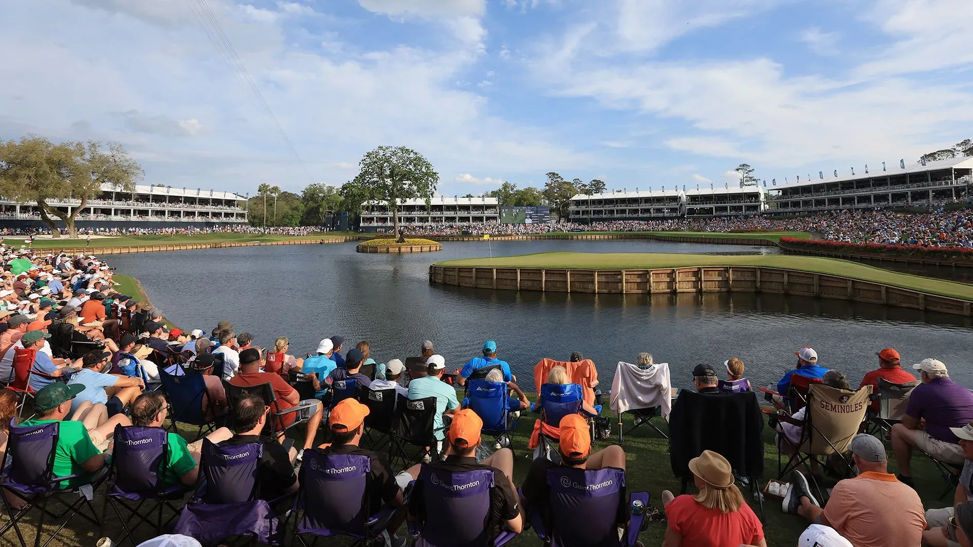 مشهد للحفرة 17 في TPC Sawgrass، حيث يتجمع الجمهور حول البحيرة المحيطة بالجزيرة الخضراء، مع أجواء تنافسية مثيرة.