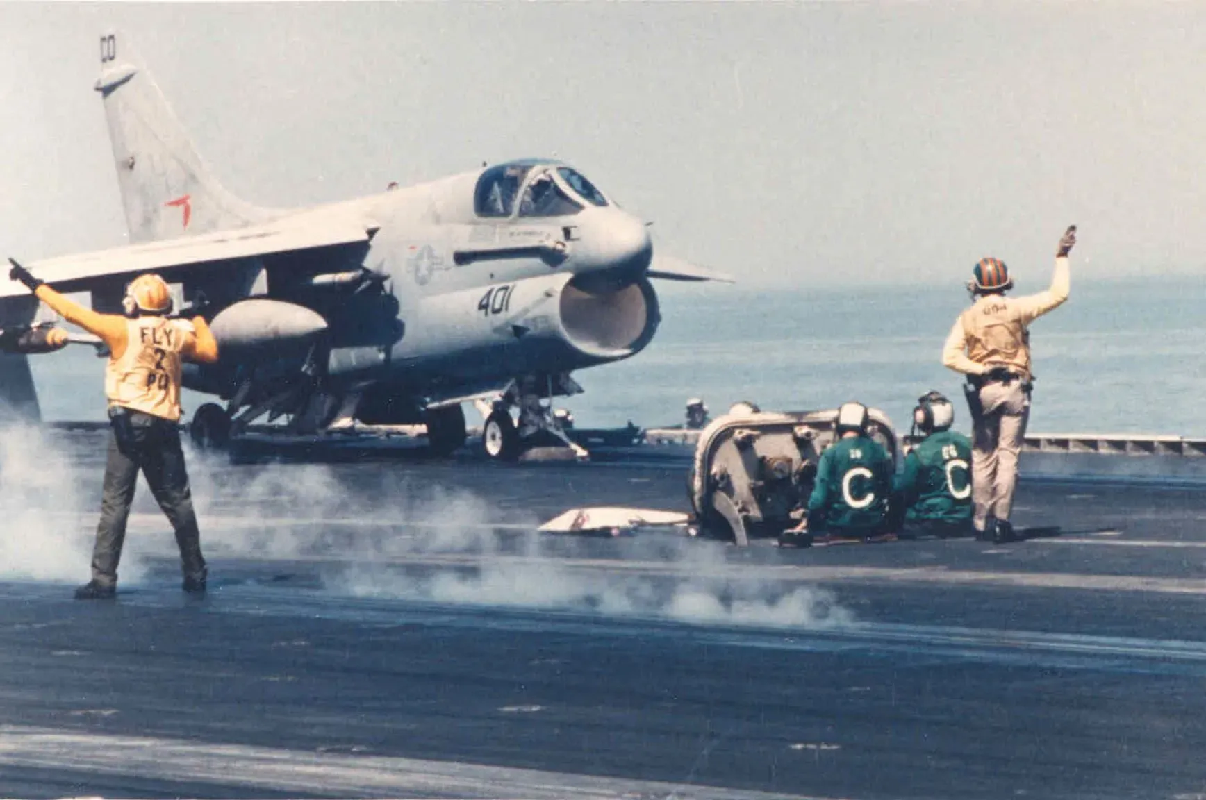 طائرة هارير أمريكية تقلع من حاملة طائرات، مع أفراد الطاقم في الخلف يتابعون العملية. تعكس الصورة النشاط العسكري خلال حرب الناقلات.