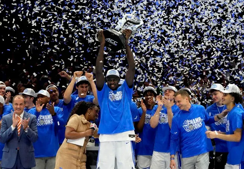 خامان مالواش، لاعب كرة السلة، يحتفل بفوز فريقه في مسابقة الدوري الأمريكي لكرة السلة، رافعًا الكأس وسط الأضواء والألعاب النارية.