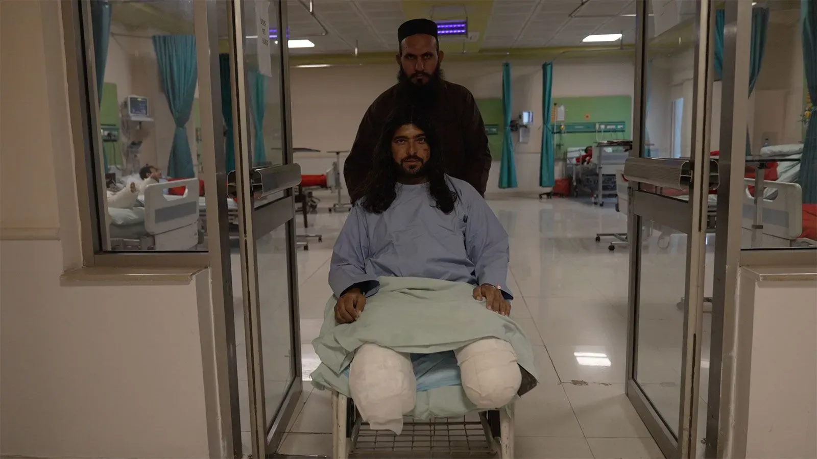 رجل مصاب يجلس على عربة طبية داخل مستشفى، بينما يرافقه شخص آخر، في سياق يعكس تأثير النزاع في المنطقة.