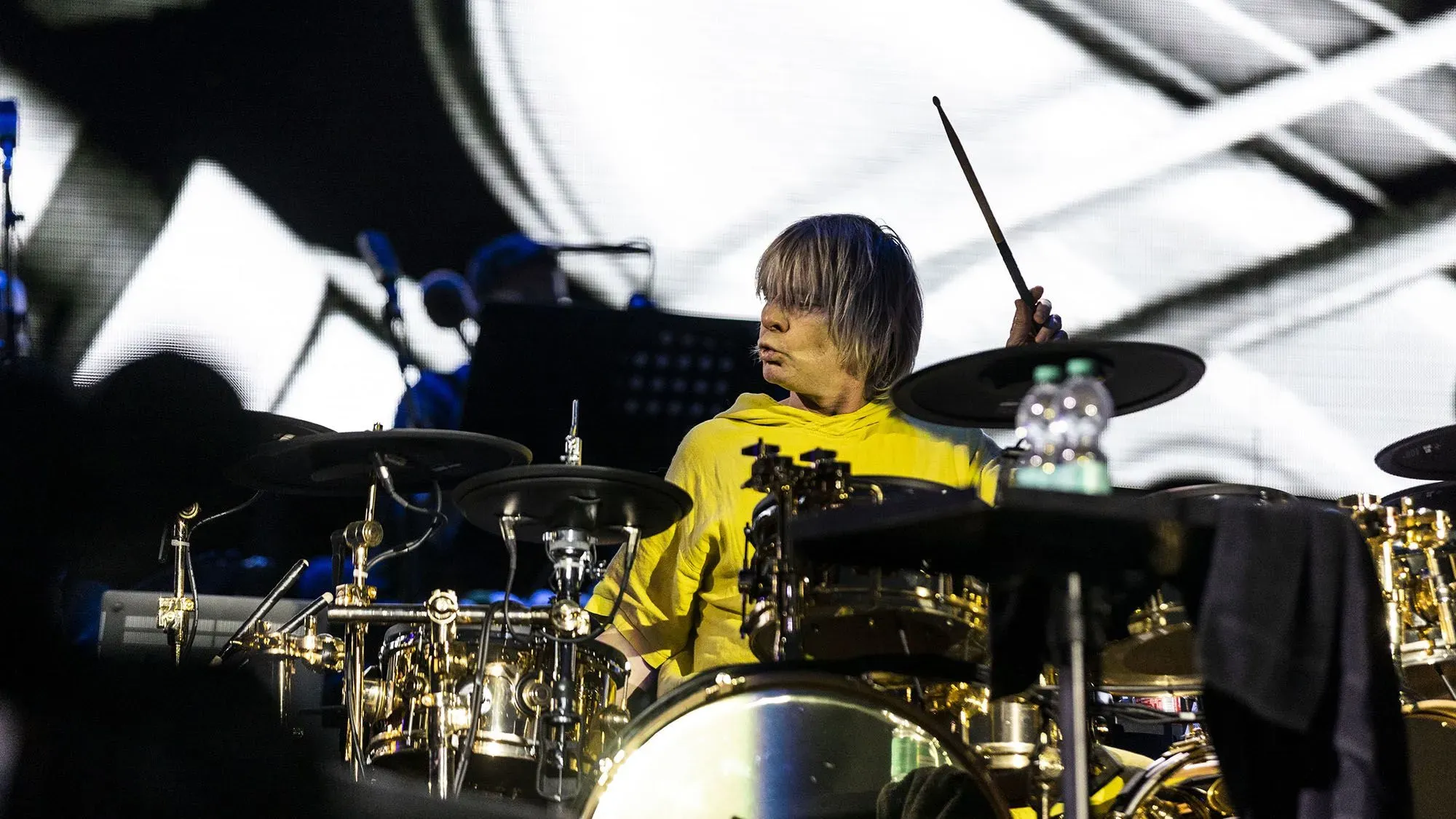 زاك ستاركي، عازف الطبول السابق لفرقة The Who، يعزف على آلته خلال عرض موسيقي. يظهر خلفه شاشة تعرض صورًا فنية.