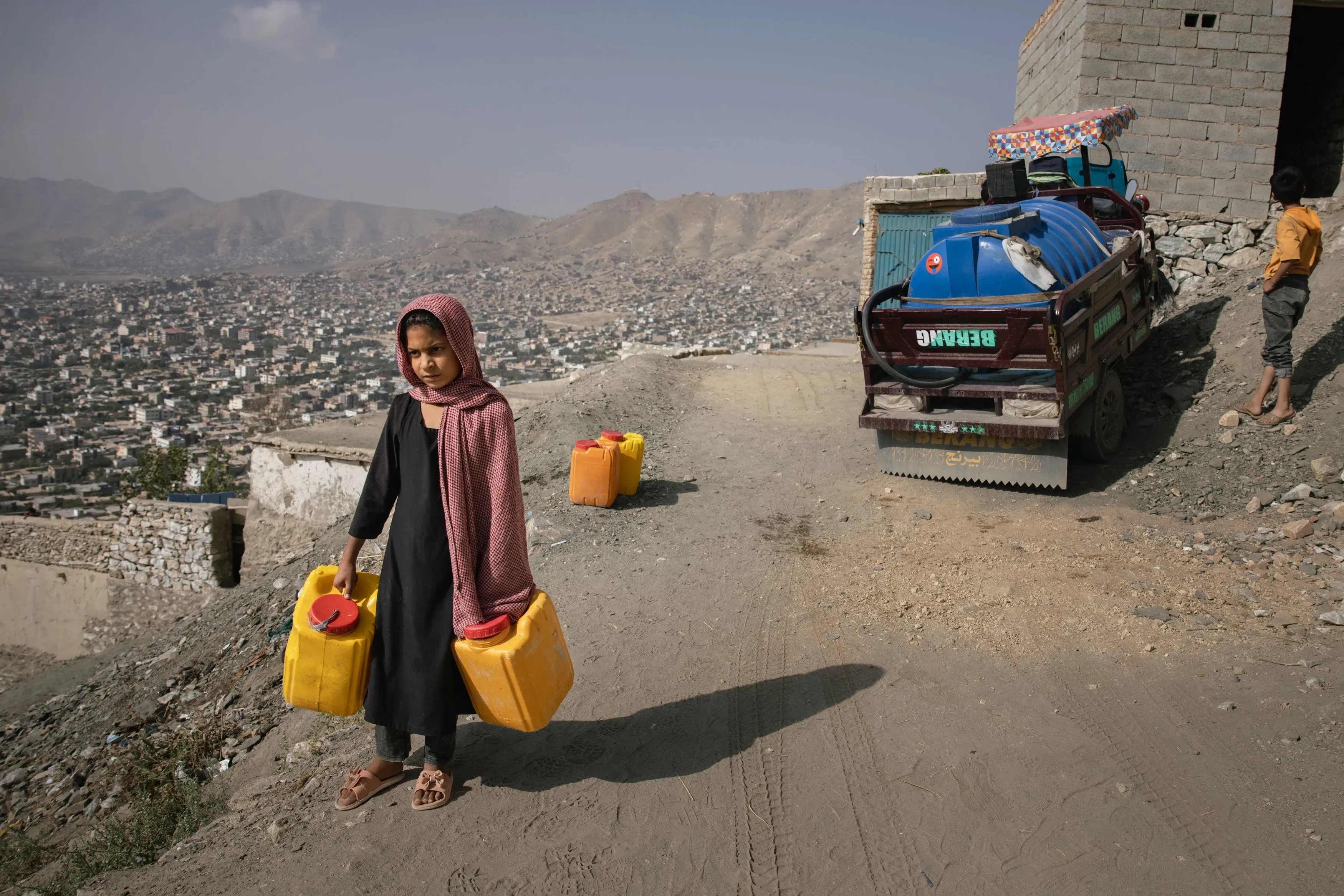 طفلة تحمل دلاءً صفراء في منطقة جبلية بكابول، تعكس أزمة المياه العالمية وتأثيراتها على المجتمعات.