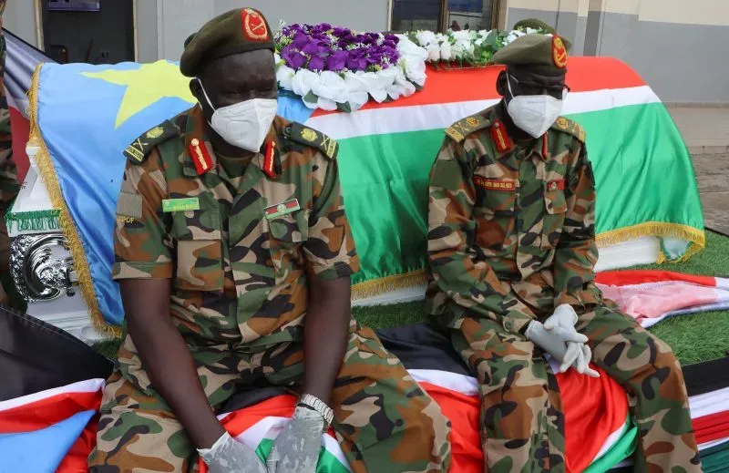 جنود يرتدون الزي العسكري يجلسون بجوار نعش مغطى بعلم جنوب السودان، مع زهور على القمة، في سياق توترات سياسية متزايدة.