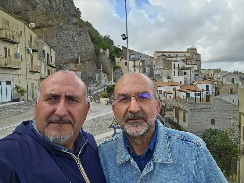 صورة لأنطونينو وكارميلو كوشيرا في بلدة صقلية، حيث يروج الأخوان لمنازل بسعر يورو واحد، مع خلفية للمنازل القديمة.