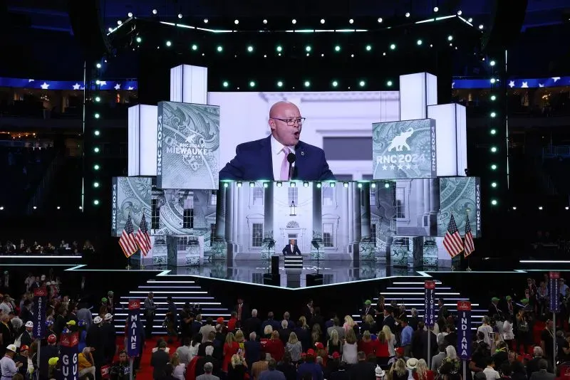 مؤتمر الحزب الجمهوري 2024، حيث يتحدث أحد المتحدثين على المنصة أمام حشد كبير، مع خلفية مميزة تتضمن رموزًا سياسية.