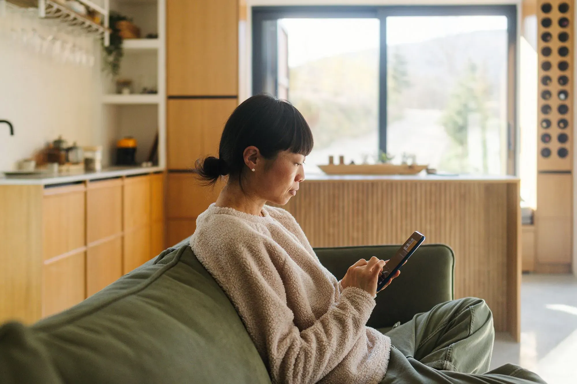 امرأة تجلس على أريكة في غرفة معيشة حديثة، تركز على هاتفها المحمول، مما يعكس تأثير وسائل التواصل الاجتماعي على الانتباه.