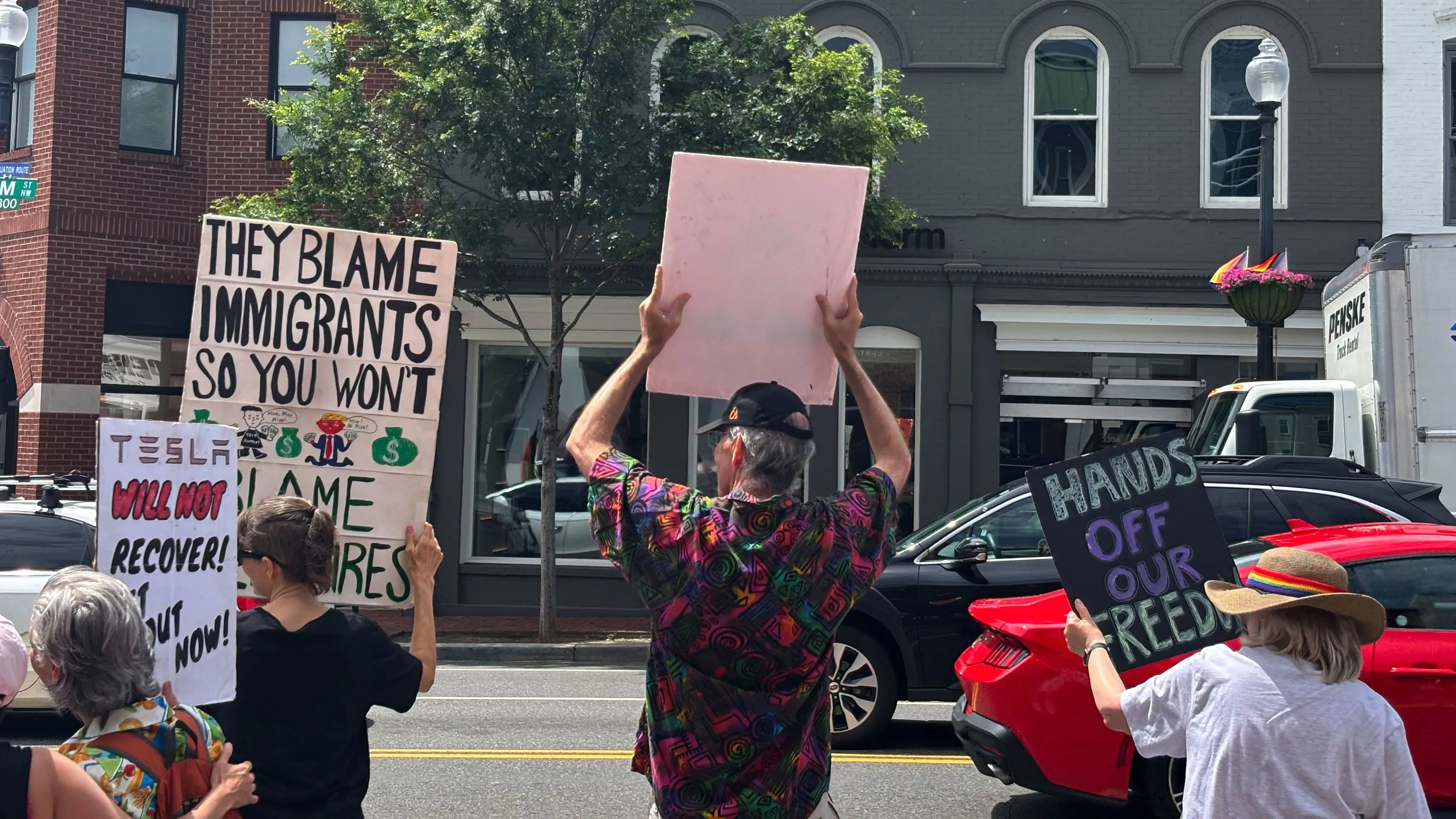 محتجون يحملون لافتات في مظاهرة خارج صالة عرض تسلا في جورج تاون، يعبرون عن معارضتهم لإيلون ماسك وسياساته.