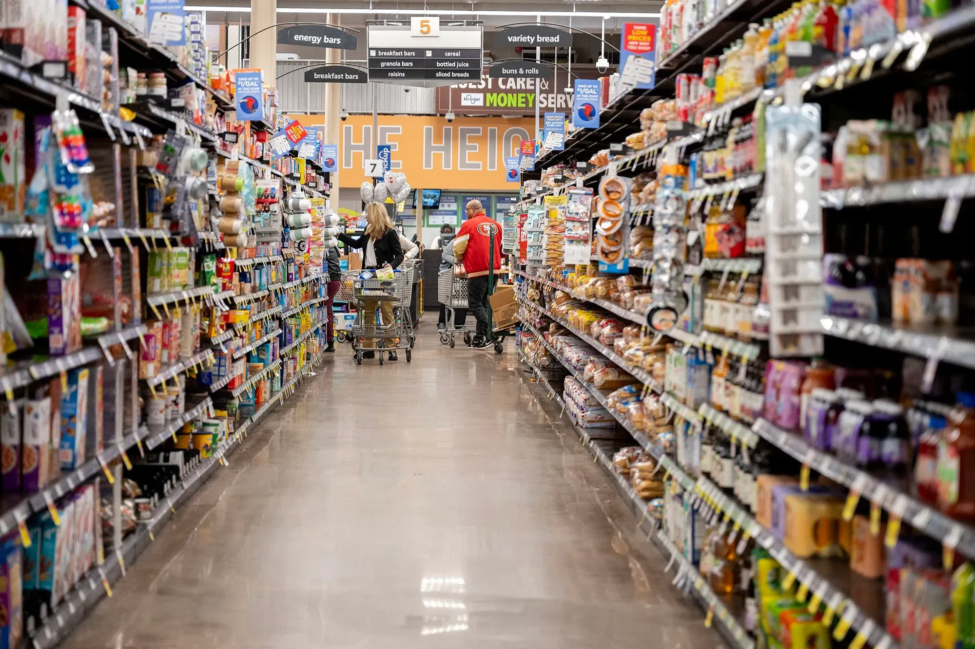 ممر في سوبرماركت يظهر متسوقين يتجولون بين الرفوف المليئة بالمنتجات، مما يعكس حالة الإنفاق الاستهلاكي في الاقتصاد الأمريكي.