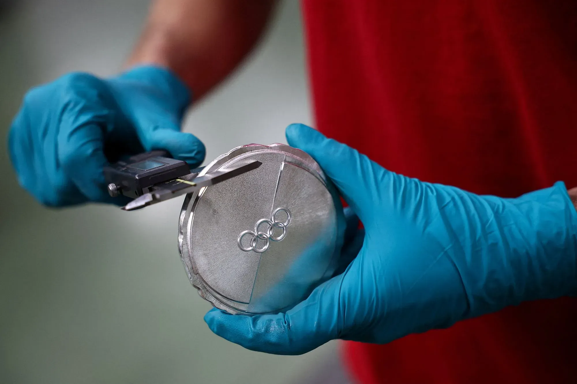 ميدالية فضية أولمبية يتم قياسها بواسطة شخص يرتدي قفازات زرقاء، مع شعار الألعاب الأولمبية مرسومًا عليها، تعكس قيمة الميداليات في الألعاب الشتوية.