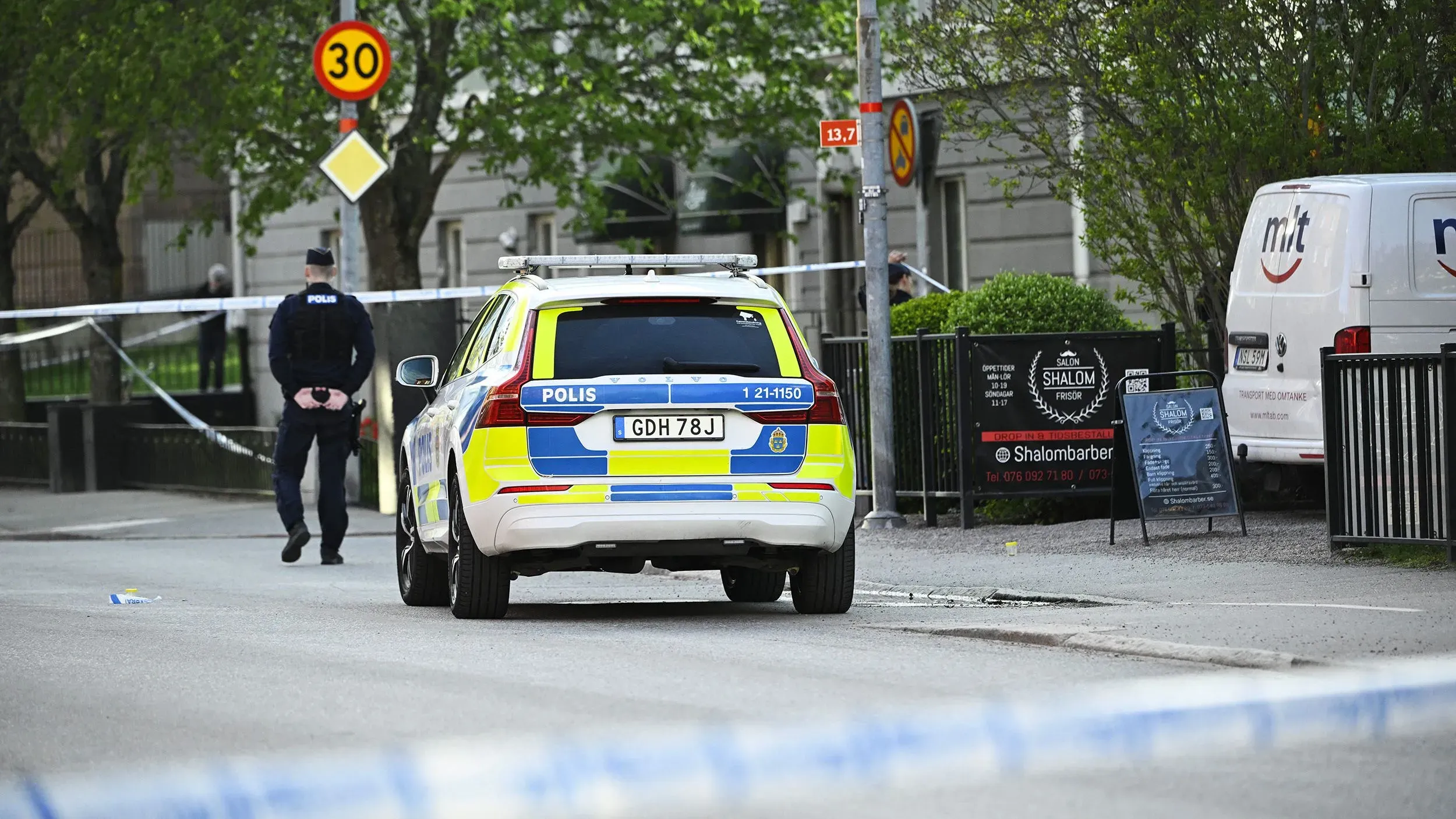 سيارة شرطة سويدية متوقفة في موقع حادث إطلاق نار في أوبسالا، مع وجود ضباط شرطة في المنطقة المحيطة.