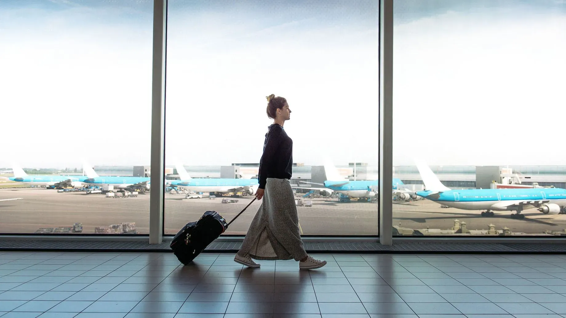 امرأة تسير في مطار، تسحب حقيبة سفر، بينما تظهر الطائرات في الخلفية، تعكس روح السفر والراحة أثناء الرحلات الجوية الطويلة.