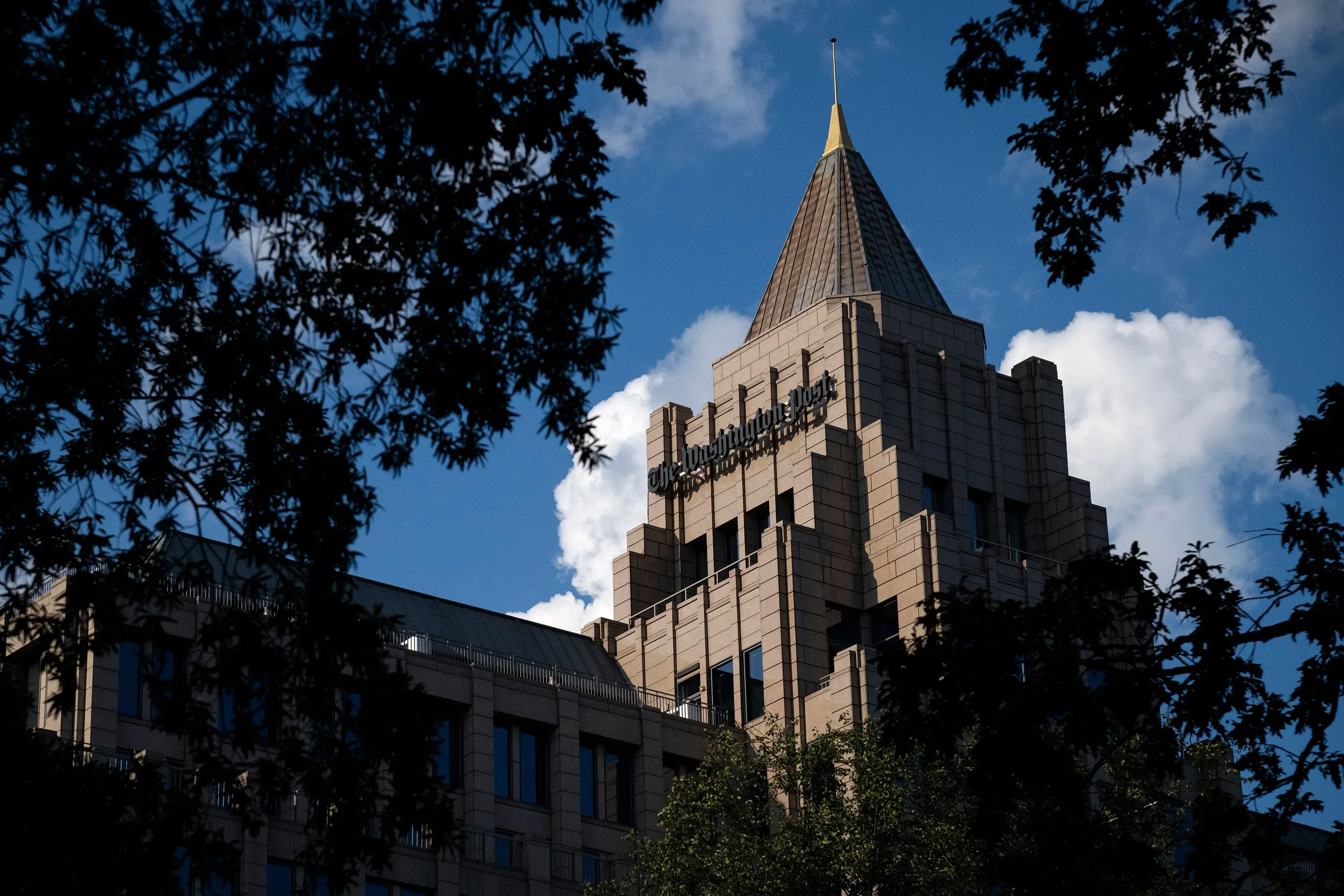 مبنى صحيفة واشنطن بوست يظهر في الصورة، مع سماء زرقاء وغيوم. يمثل الحدث المداهمة غير المسبوقة لمكتب الصحيفة.
