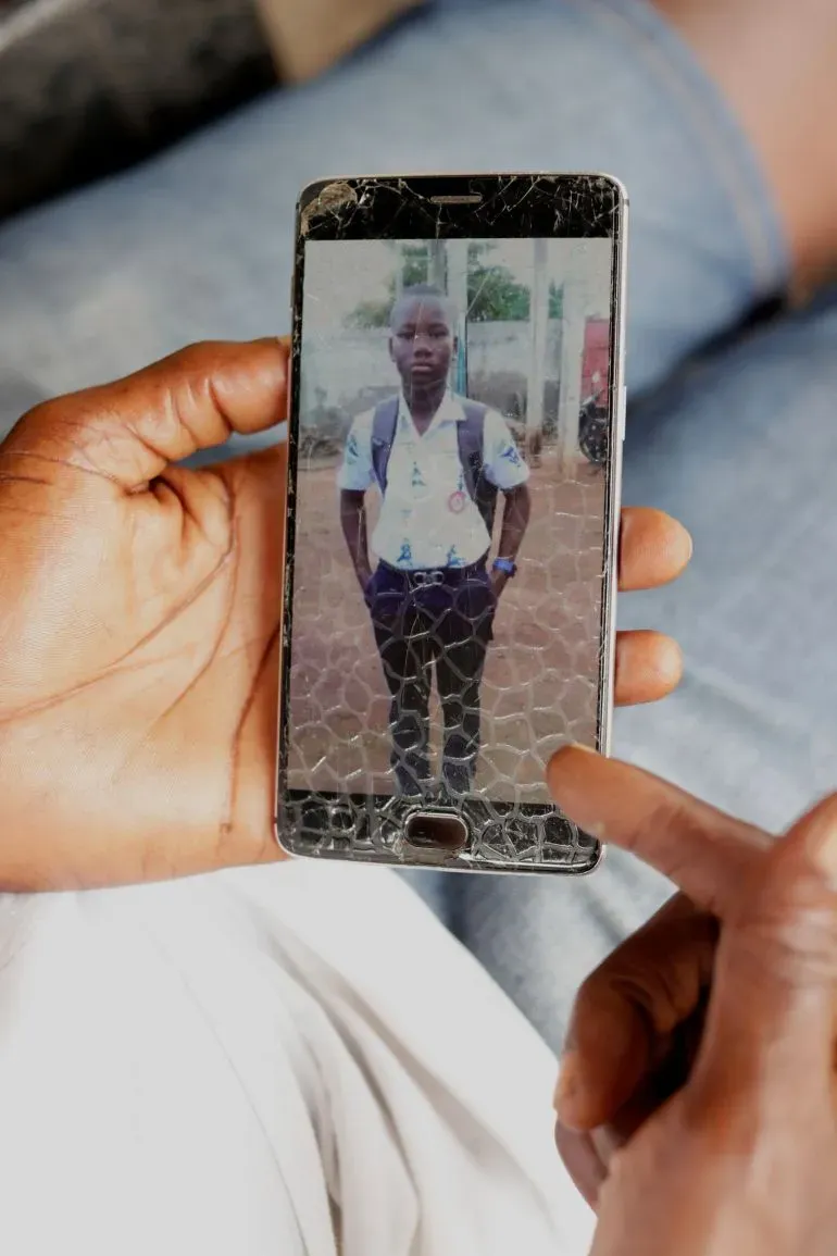 شخص يحمل هاتفًا محمولًا يظهر صورة شاب يرتدي زي المدرسة، مع وجود شاشة مكسورة، تعبير عن القلق في سياق الاحتجاجات بتوغو.