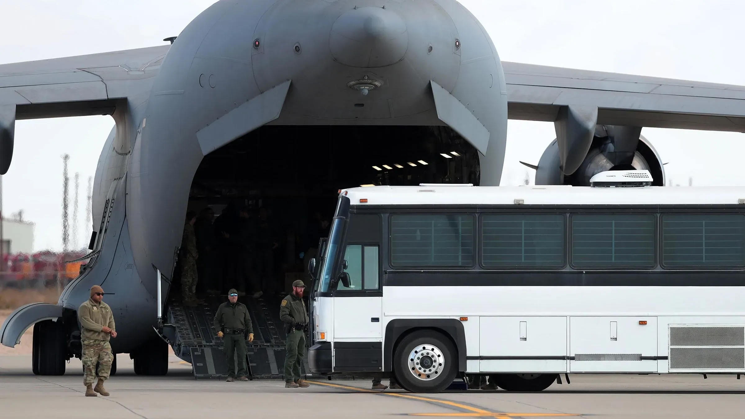 طائرة C-17 تابعة للقوات الجوية الأمريكية تفتح أبوابها لنقل المهاجرين إلى ليبيا، مع وجود جنود ومركبة بالقرب منها.