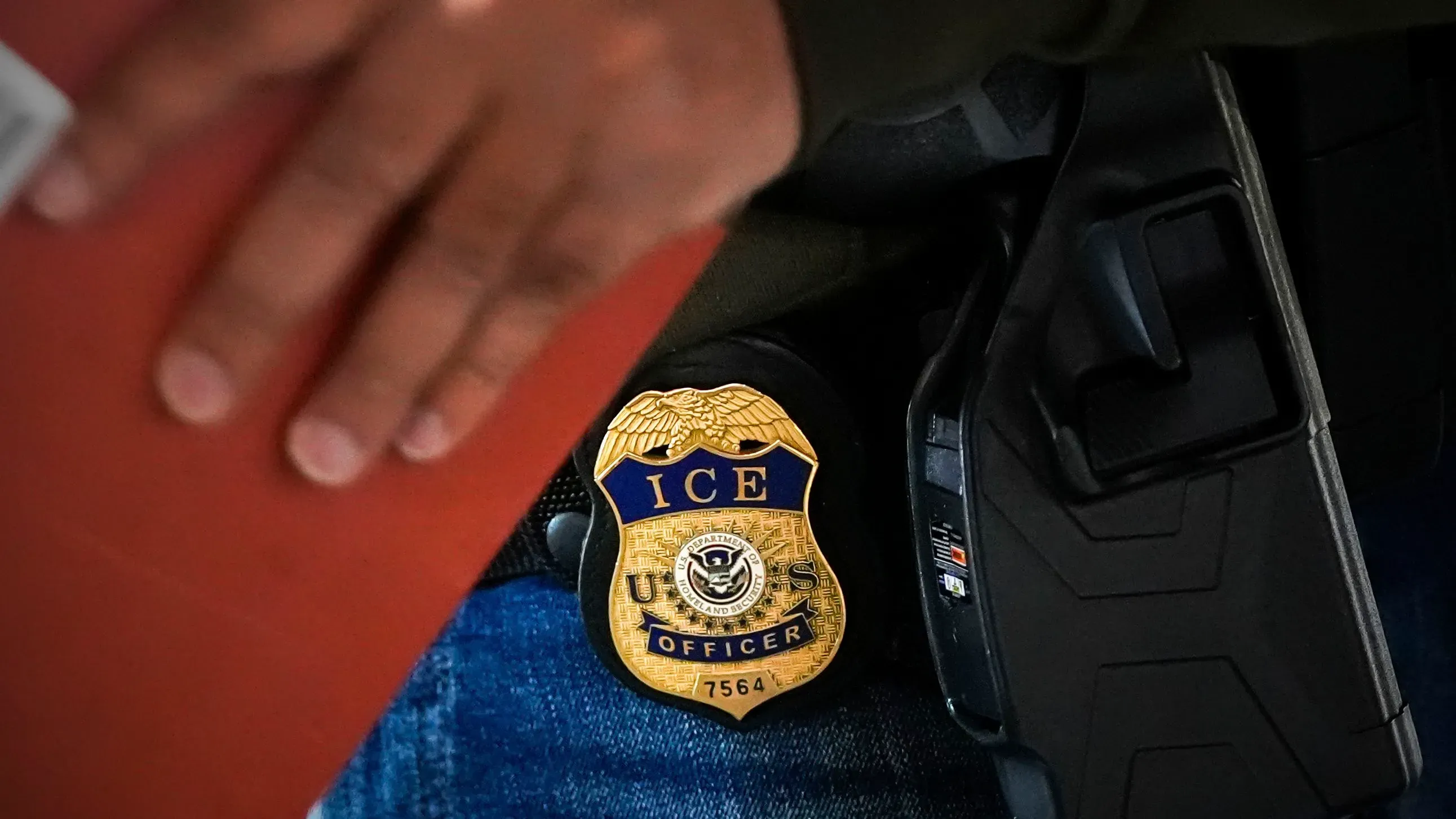 شعار وكالة الهجرة والجمارك الأمريكية (ICE) على حزام ضابط، مع التركيز على إجراءات احتجاز الأطفال المهاجرين.