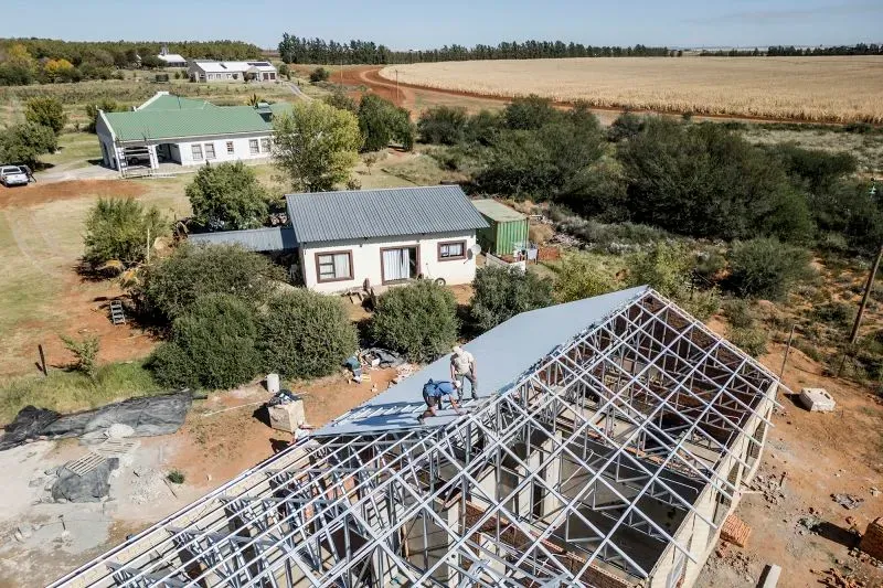 مجموعة من الأشخاص يعملون على بناء منزل في مستوطنة أورانيا بجنوب أفريقيا، حيث يسعون لتحقيق الاستقلال الذاتي.